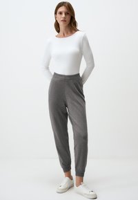 Graue Jogginghosen mit geripptem Bund und Bündchen, kombiniert mit einem enganliegenden weißen Langarmoberteil. Die Schuhe sind weiß mit subtilen Details.
