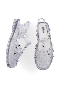 Sandalias de plástico transparente con un diseño de punta cerrada, que presentan tachuelas decorativas, una correa ajustable en el tobillo y una suela transparente texturizada.