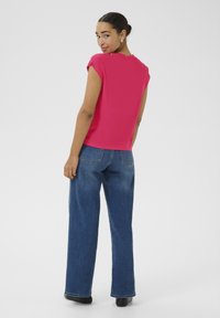 Kurzärmlige pinke Bluse, kombiniert mit weit geschnittenen blauen Jeans. Glatter Stoff, schlichter runder Halsausschnitt und dezente Schulterdetails.