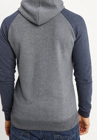 Bluza z kapturem, charakteryzująca się szarym korpusem i ciemnoszarymi rękawami typu raglan, wykonana z miękkiego materiału, z elastycznym wykończeniem na dole i przy mankietach.