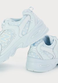 Vaaleansiniset urheilukengät, joissa on valkoisia pilkkuja, verkkokangas, teksturoitu pohja ja "ABZORB" -merkkitunnus kannassa.