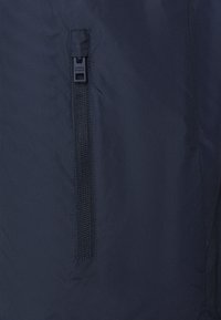 Marintröja i tyg med en slät textur och en vertikal dragkedja med svart dragflik längs sömmen på sidan.