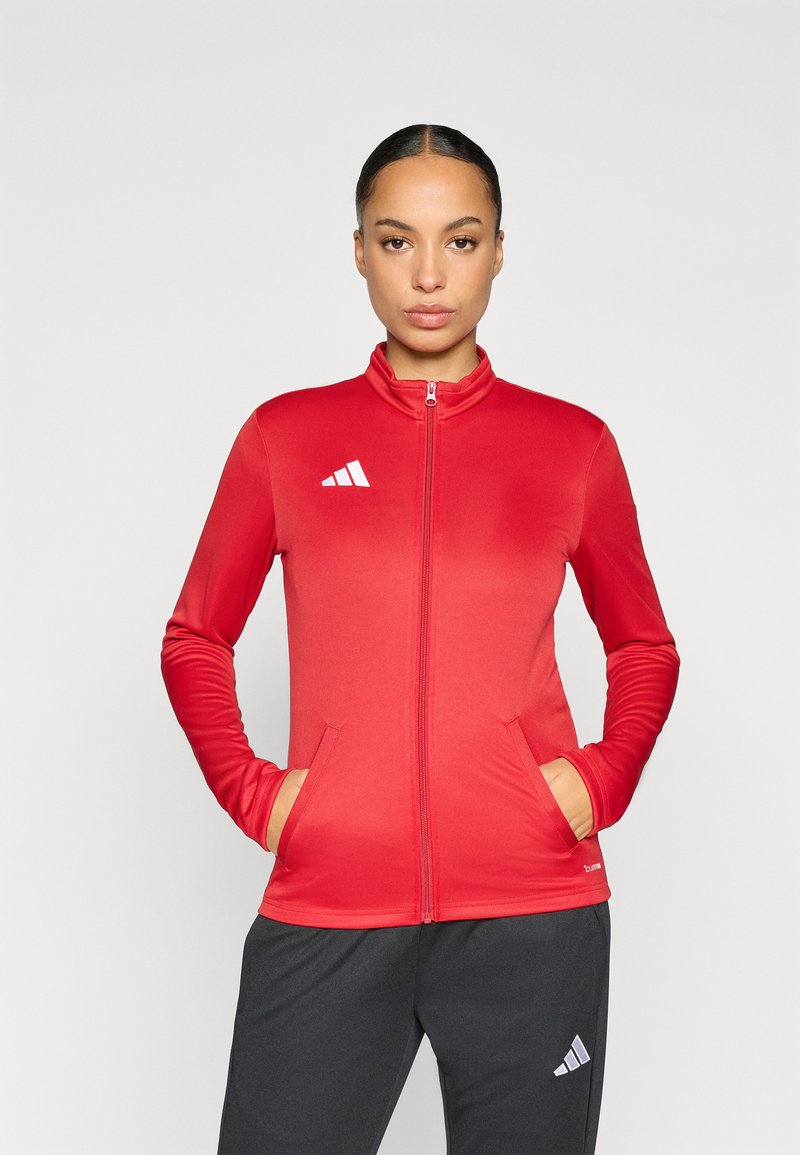 Αθλητικό κόκκινο μπουφάν με φερμουάρ, ψηλό γιακά, μακριά μανίκια και δύο πλαϊνές τσέπες· διαθέτει λευκό λογότυπο στην πάνω αριστερή πλευρά.