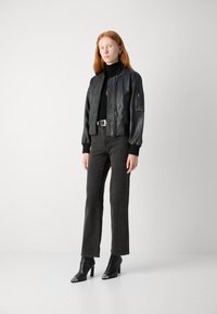 Chaqueta bomber de cuero negro con puños y cuello acanalados, combinada con jeans de tiro alto en gris oscuro y botines negros de punta.