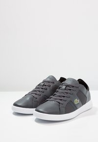 Baskets en cuir gris avec côtés en mesh, semelle en caoutchouc blanche et accents texturés. Comprend le logo LACOSTE et un design classique à lacets.