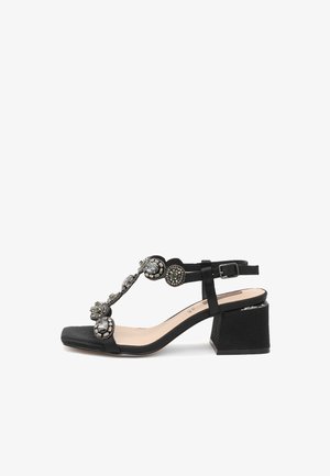 Sandali neri con tacco a blocco. Presentano un design a T decorato con pietre decorative e una cinghia alla caviglia regolabile. Texture morbida.