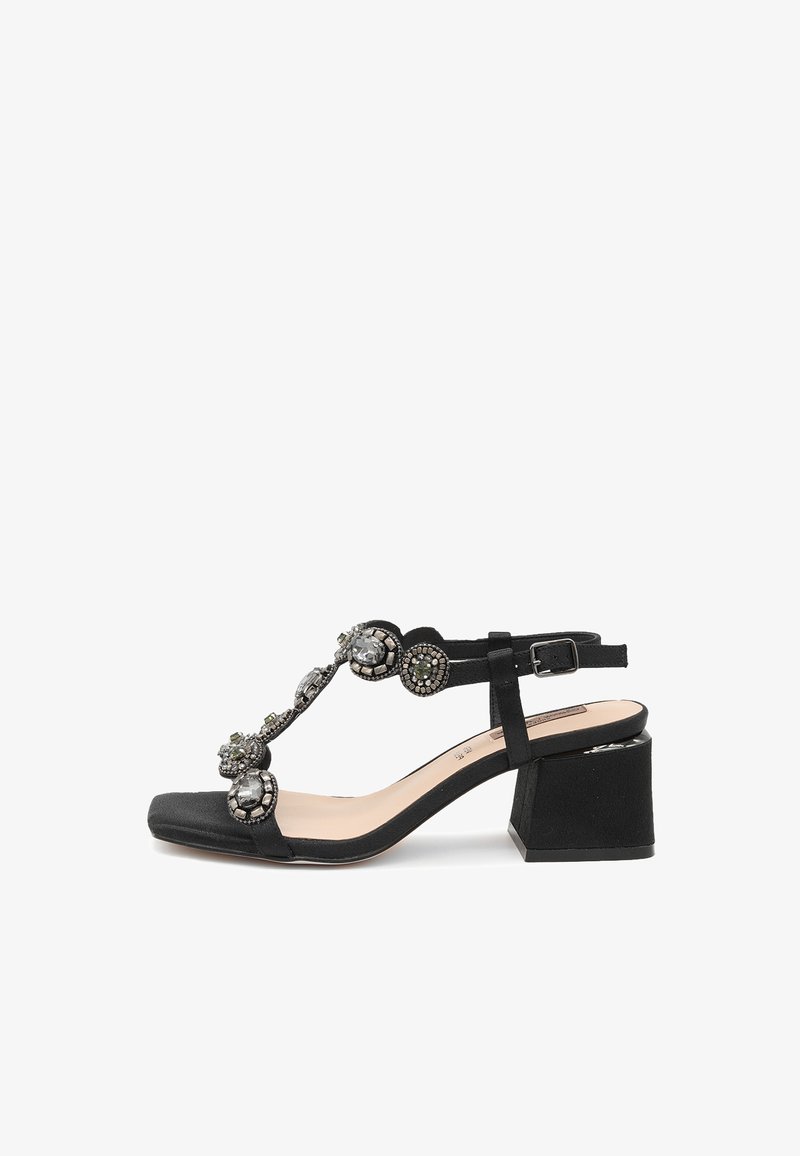 Sandali neri con tacco a blocco. Presentano un design a T decorato con pietre decorative e una cinghia alla caviglia regolabile. Texture morbida.