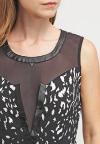 Svart och vit klänning med ett genomskinligt topp, med en texturerad leopardtryck, satindetaljer och en V-ringning.
