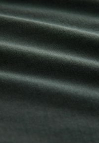Țesătură de culoare verde închis cu o textură netedă și moale, prezentând ondulații și pliuri subtile, indicând un material ușor, potrivit pentru diverse utilizări.