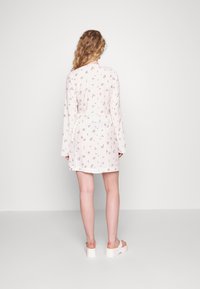 Vestido de estampado floral en tela rosa claro, con mangas largas y cintura ceñida, con un dobladillo corto, combinado con sandalias plataforma blancas.