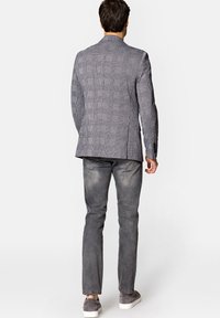 Szary marynarka w kratę z wyciętymi klapami, teksturowany materiał i dwa tylne rozcięcia, zestawiona z jasnoszarymi dżinsami i szarymi sneakersami.