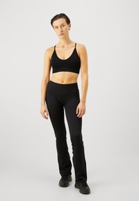 Sostén deportivo negro con tirantes finos, combinado con leggings negros de tiro alto. Ambos tienen una textura suave y un ajuste aerodinámico. Zapatillas negras.