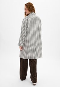 Houndstooth patroonjas in grijs en wit, lange mouwen, kraag en zijsplitten, in combinatie met bruine corduroy broek.