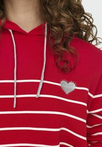 Felpa a righe rosse con cordini argentati. Presenta righe orizzontali bianche e un ricamo a forma di cuore argentato sul lato sinistro del petto.