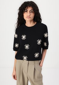 Maglione nero a maglia con maniche corte, caratterizzato da ricami di fiori color crema. Il design presenta un collo a coste e una vestibilità morbida.