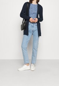 Námořnický dlouhý kardigan přes modro skvrnitý top, v kombinaci se světlemodrými džíny s vysokým pasem a bílými teniskami. Černá crossbody taška je součástí.