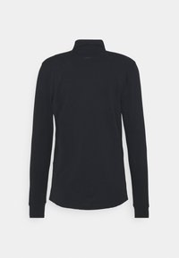 Pitkähihaista mustaa poolopaitaa, joka on valmistettu puuvillasta, ja siinä on taitettu kaulus ja hihansuut, sileä rakenne sekä suora helma takana.