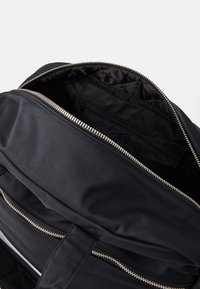 Sac à dos en tissu noir avec une ouverture zippée sur le dessus. L'intérieur présente une texture lisse et une petite poche zippée pour l'organisation.