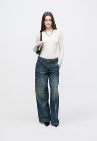 Bukser med vide ben i mørkeblå denim, der har en fadet tekstur, lappesøm-detaljer og høj talje. Kombineret med en tætsiddende langærmet top.