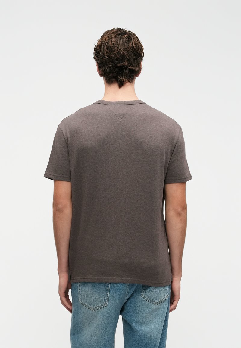 Mand set fra ryggen iført en ensfarvet mørkegrå kortærmet t-shirt og lyseblå jeans foran en hvid baggrund.