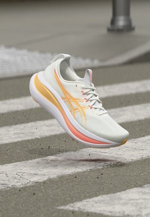 Chaussure de course blanche et orange avec lacets flottant au-dessus d'un passage piéton texturé sur chaussée en asphalte.