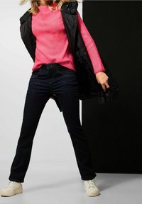 Figurformad rosa ribbad tröja under en svart pufferväst, samsatt med mörkblå denimjeans och vita sneakers. Strukturerad tyg och avslappnad stil.