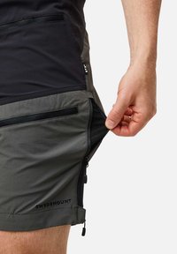 Shorts met een zwart bovenste gedeelte en een grijs ondergedeelte, voorzien van ritszakken en een logo op de zoom. Vloeiende, lichte stof.