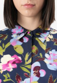 Blomstrete skjorte med marineblå bakgrunn og rosa og blå blomsterdesign, en klassisk krage og knappelukking ved halsen.