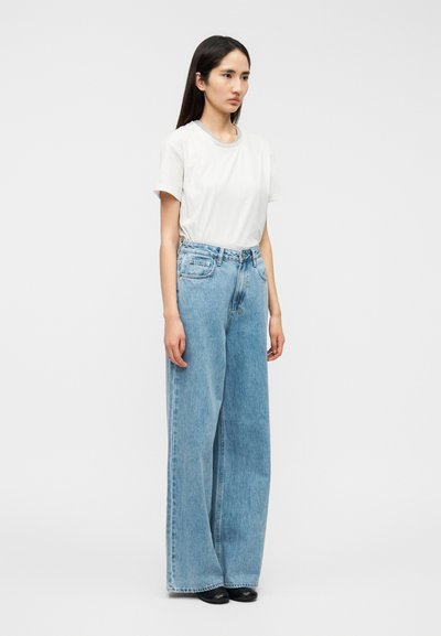 Λευκό μπλουζάκι κοντομάνικο και ανοιχτό μπλε τζιν παντελόνι με φαρδιά πόδια. Το τζιν διαθέτει εμπρόσθιες τσέπες και ψηλή μέση, αντίθετη ραφή, διακριτική ξεβάμματα.