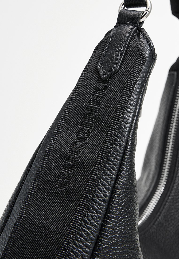 Sac à main en cuir noir avec une finition texturée, présentant un design élégant, une fermeture éclair et une sangle en tissu arborant un logo en relief.