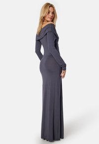Robe longue ajustée en tissu gris doux, dotée d'un décolleté drapé  hors des épaules et de longues manches, avec une silhouette fluide et élégante.