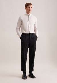Camicia button-up grigia chiara con una texture a costine, abbinata a pantaloni neri plissettati e scarpe in pelle nera. Design semplice e su misura.