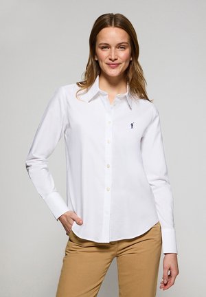 Witte button-up shirt gemaakt van katoen met lange mouwen, voorzien van een marineblauw logo op de borst, gecombineerd met kaki broek.