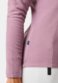 Lichtpaarse fleecjacket met lange mouwen, gestructureerd oppervlak en een zijnaad met een klein detail van de Zweedse vlag nabij de zoom.