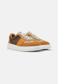 Sneakers con lacci, con una parte superiore in pelle marrone chiaro e marrone scuro, accentuate da dettagli arancioni e tessuto beige. Suola in gomma bianca spessa e dettagli di cucitura a contrasto.