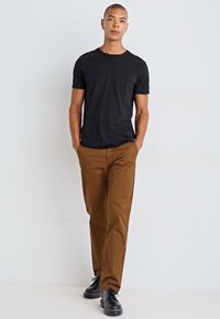 Black short-sleeve t-shirt, brown straight-leg pants, and black shoes. Smooth fabric texture with a fitted silhouette. Simple design.