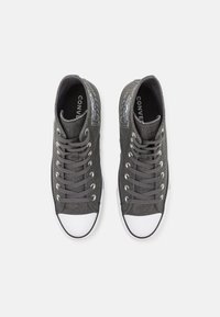 Visoke teniske u tamno sivoj platnu s belim gumiranim vrhom. Ima sive vezice, srebrne oči i detalj loga blizu zapešća.