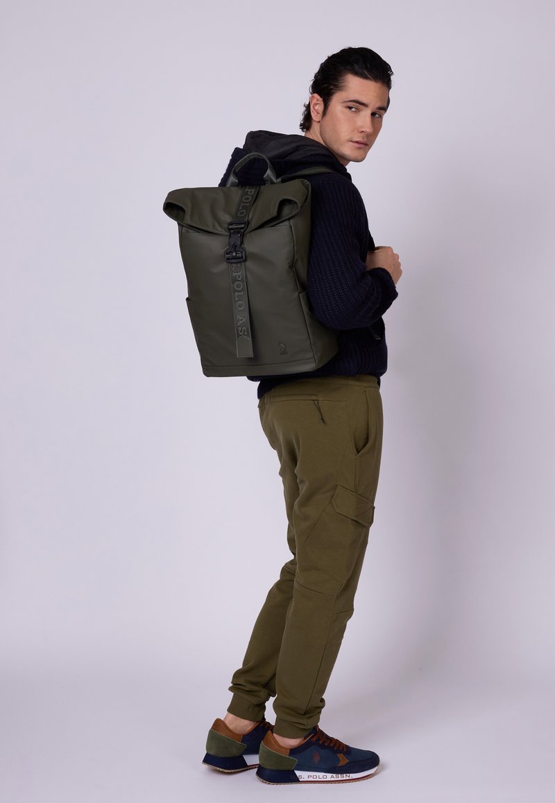 Rucsac de tip roll-top de culoare verde măslinie, cu bretele ajustabile, închidere cu cataramă și un exterior neted, rezistent la apă; detaliu cu logo pe lateral.