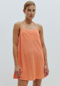 Ein ärmelloses A-Linien-Kleid aus strahlendem Korallestoff, mit dünnen Trägern und einer lässigen Passform. Glatte Textur mit einem einfachen, ununterbrochenen Design.
