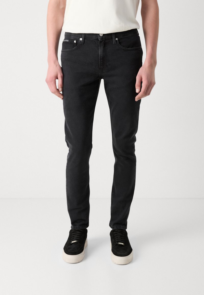 Czarne dżinsy o dopasowanym kroju. Posiadają pięć kieszeni, srebrne elementy i gładką teksturę. Noszone z czarnymi trampkami.