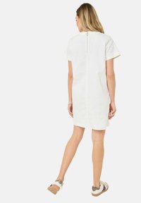 Weißes Kurzarmkleid mit einem Reißverschlussdetail hinten, das einen geraden Schnitt und eine glatte Textur aufweist. Kombiniert mit beigen Akzenten an den Schuhen.