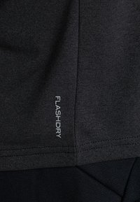 Černá atletická tkanina s hladkým povrchem a viditelnými šedými štítky "FLASHDRY". Zaměření na materiály a funkční designové prvky.