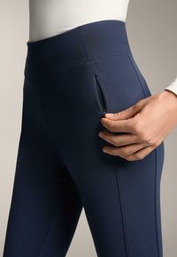 Tengerészkék, magas derekú leggings, rugalmas anyagból, oldalán cipzáras zsebbel és vízszintes varrásdíszítéssel.