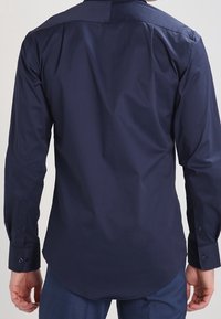 Marineblaues Langarmhemd mit glatter Textur, abgerundetem Saum und Knopfmanschetten. Verfügt über einen klassischen Kragen und eine taillierte Passform.