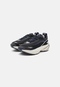 Melnas un tumši zila sieta sporta apavi ar zamšādas akcentiem, ar biezu baltu zoli, apaļu purngalu un izteiktu zīmola logo sānos.