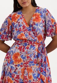 Cvečni zavitek obleka s kratkimi letečimi rokavi, živahnimi rdečimi, oranžnimi in modrimi cvetovi na svetlem ozadju, z opasanjem v pasu.