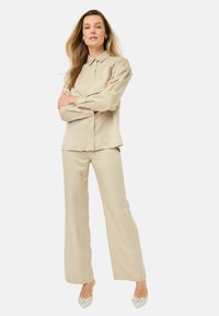 Chemise en satin beige et pantalon large assorti, avec un col et un léger brillant, accompagnés de talons embellis.
