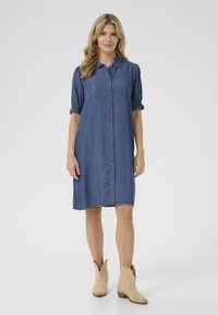 Rochie din denim cu mâneci scurte bufante, deschidere cu butoane și margini tivite. Purtați cu cizme cowboy bej pentru contrast.
