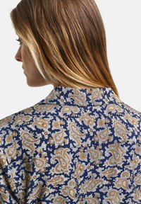 Bluză cu model paisley albastru, cu accente aurii și albe, având un guler clasic și o textură moale a materialului.
