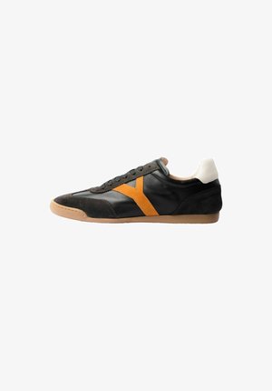 Zwarte lage sneaker met donker suède accenten, oranje zijstreep, witte hielstrook en lichtbruine rubberen zool, gezien vanaf de linkerkant.